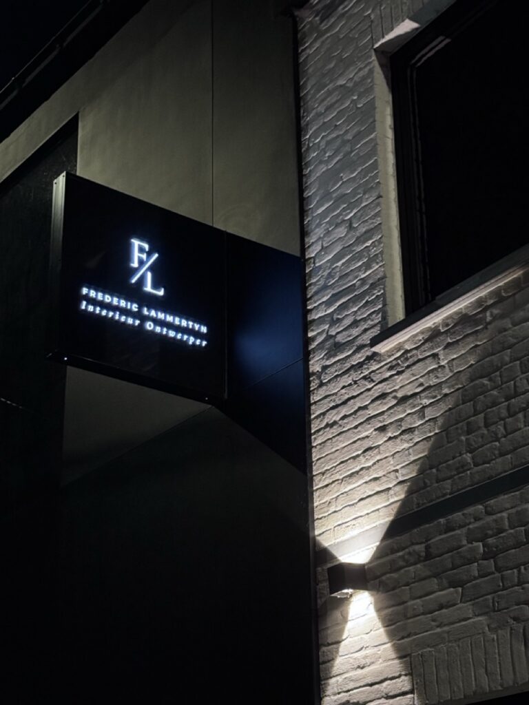 bord met logo en naam van interieurarchitect Frédéric Lammertyn aan gevel in donkere buitenomgeving